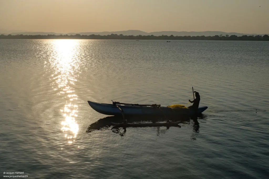 Silhouette de barque et pêcheur traditionnel au Sri Lanka en contre-jour au coucher du soleil, photographie de paysage par [Jacques Hamard