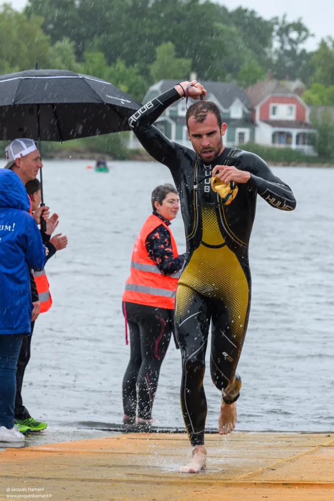Transition natation-vélo : athlète sortant de l'eau et retirant sa combinaison néoprène.